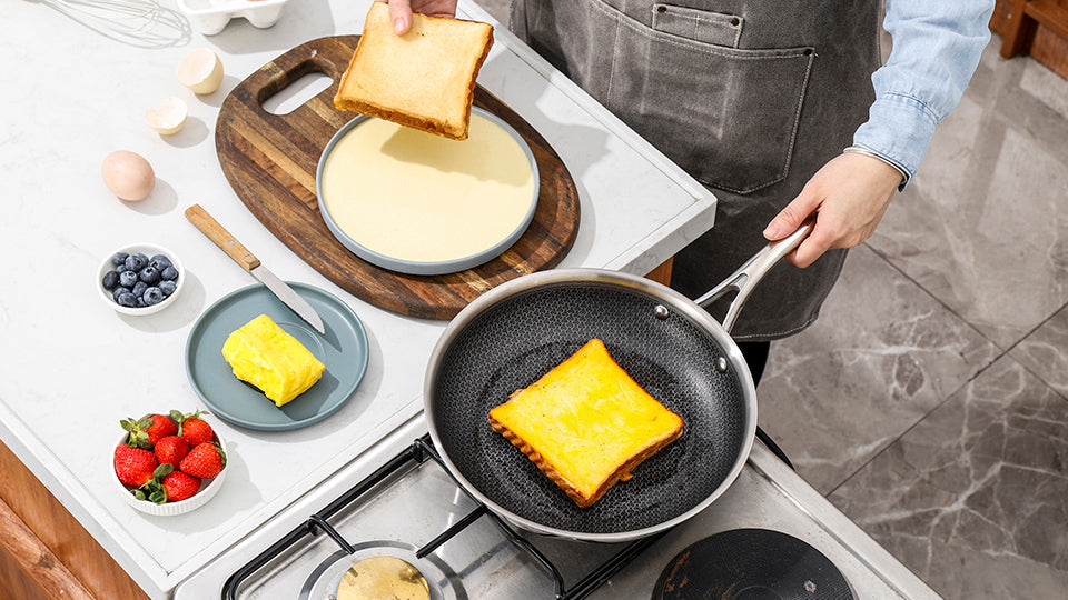 Golden French toast cooking in Deluxe Cookware non-stick pan with fresh berries and batter on kitchen counter