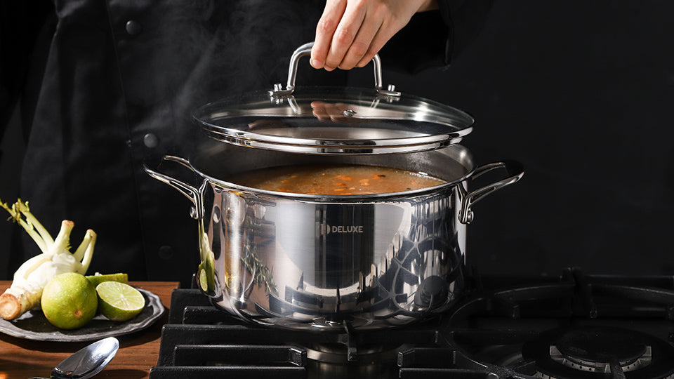 Stainless steel Dutch oven simmering soup on a stovetop with lid being lifted